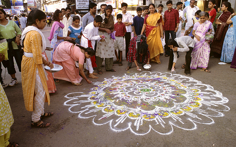 Frauen und Kinder malen mit Pulvern ein Ornament (Rangoli) 